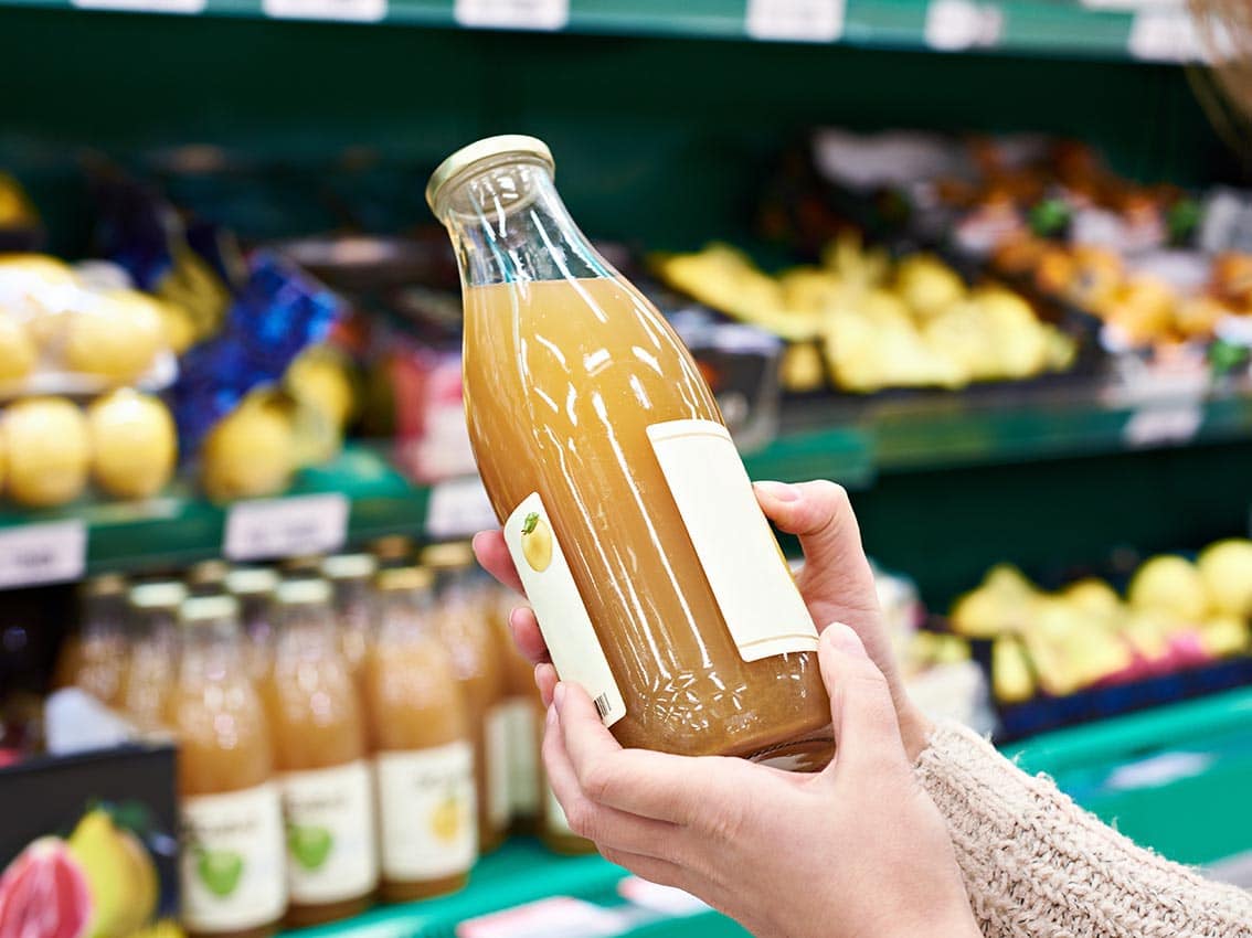 Mains avec une bouteille de jus de pomme frais en magasin - Étiquettes Autocollantes Imprimées